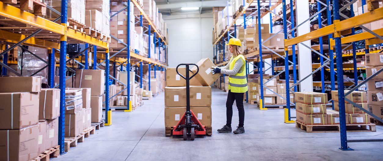 Young female warehouse worker loading up a pallet truck with boxes.