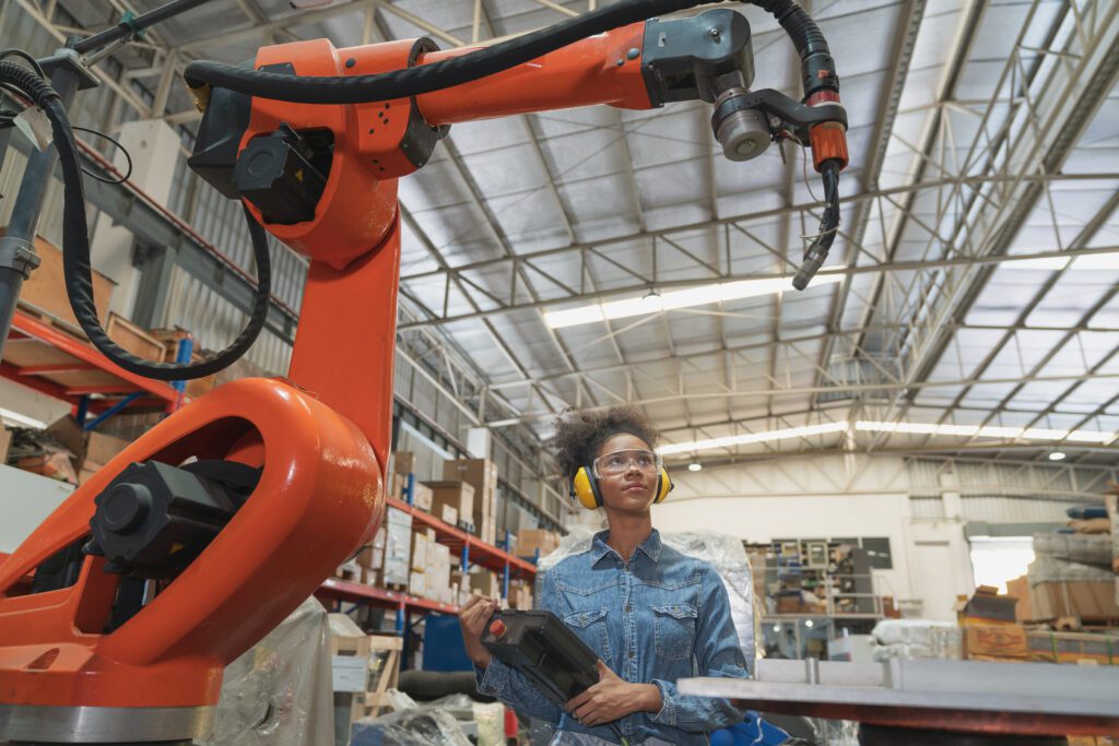 Young African American female engineer operating welding robot arm machine in warehouse factory.Professional technician automation robotic industrial